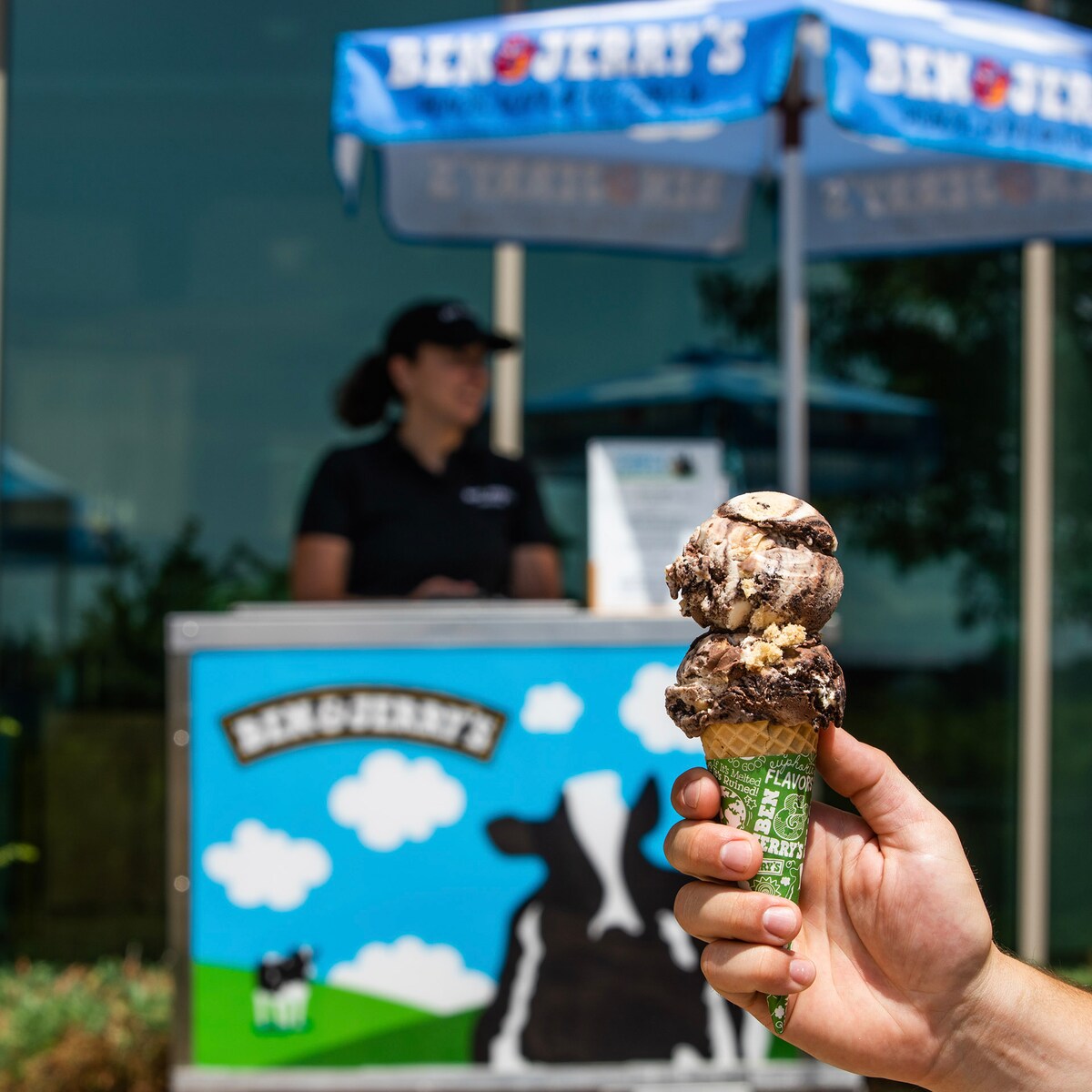 Hand holding an ice cream cone in front of a catering cart